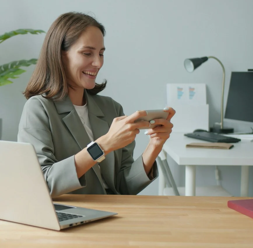 Colaboradora sorrindo enquanto usa o celular em uma mesa de escritório