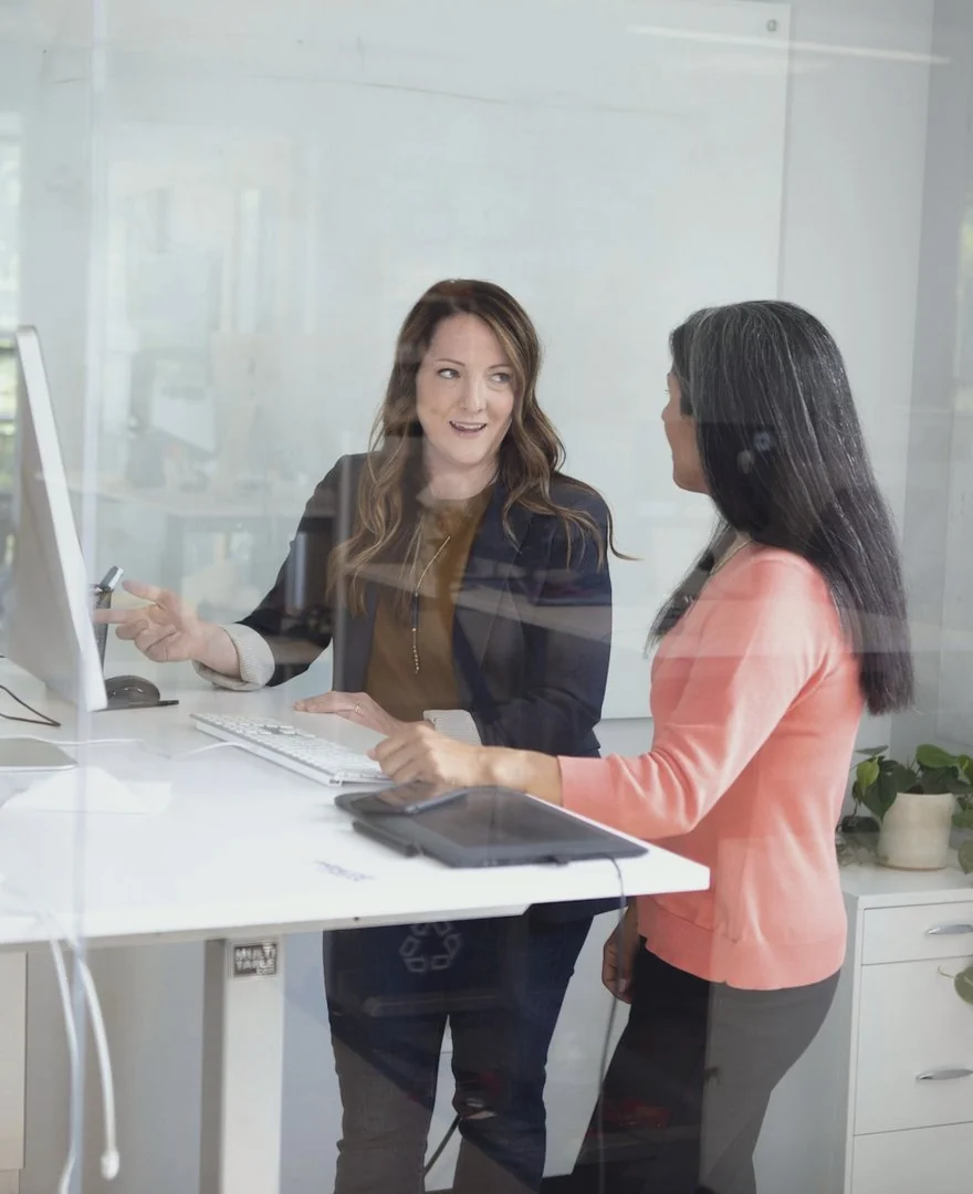 Duas colegas conversando diante de um computador no escritório