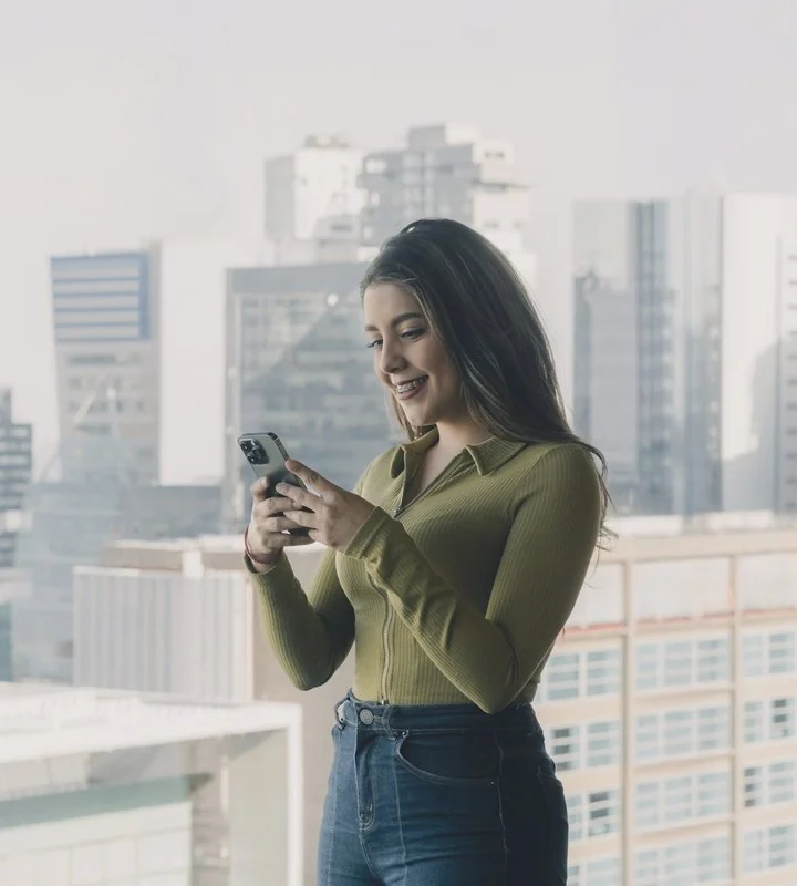 Mulher usando o celular perto de uma janela com vista da cidade